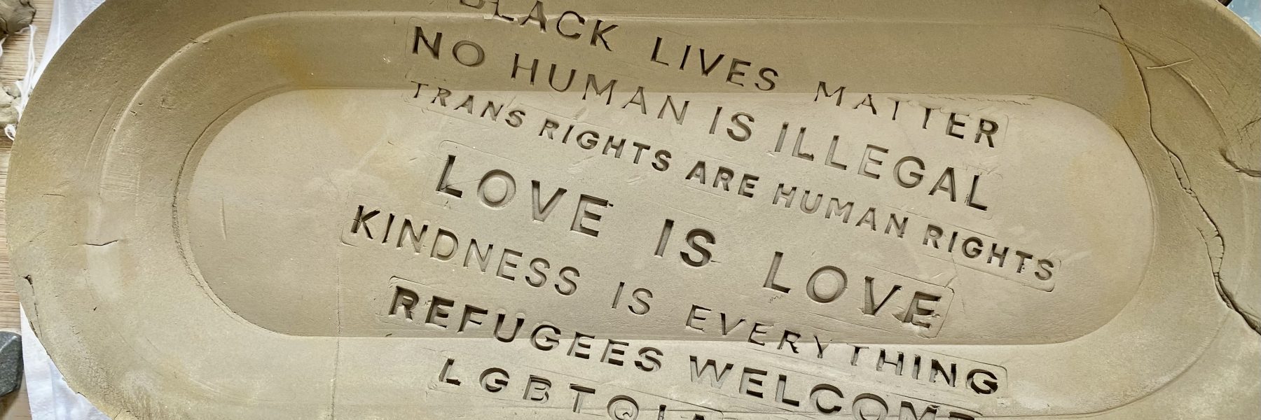 A clay pot with text written across it: No Human is Illegal, Black Lives Matter, Ban Bigots Not Books, Love is Love, Kindness is Everything 