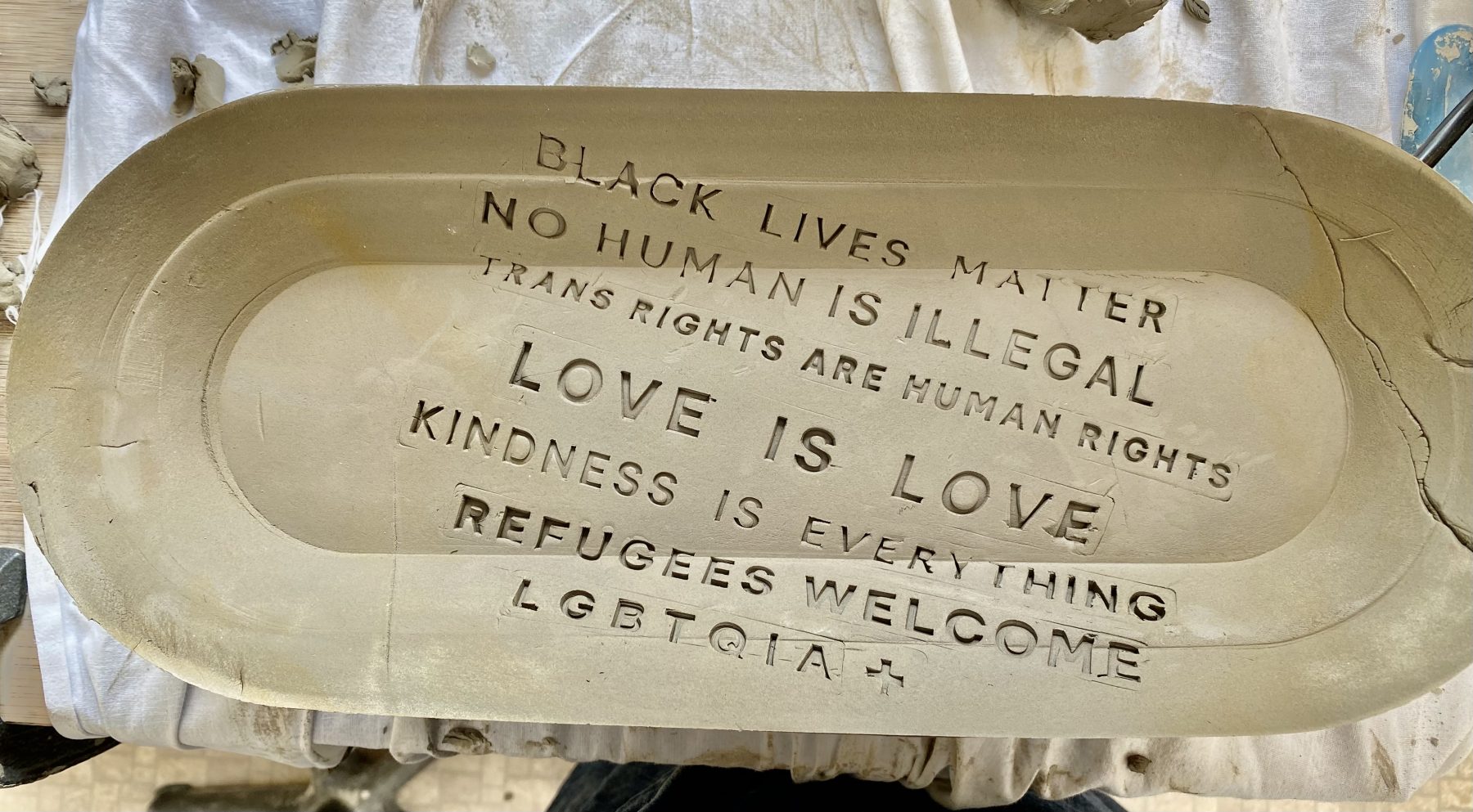 A clay pot with text written across it: No Human is Illegal, Black Lives Matter, Ban Bigots Not Books, Love is Love, Kindness is Everything