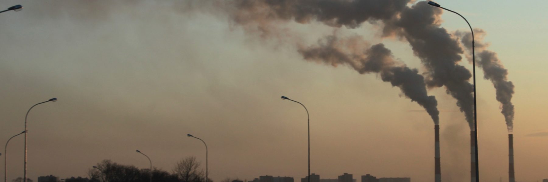 Three tall industrial chimneys with smoke billowing